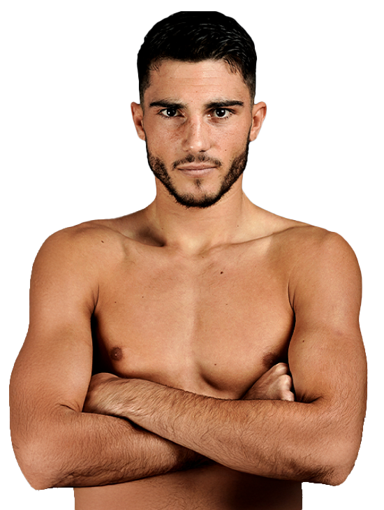 A bare-chested man with short dark hair and a beard stands with his arms folded, looking directly at the camera against a plain light background.