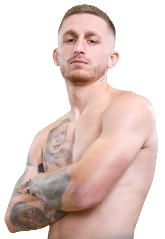 A bare-chested man with short hair and tattoos on his arms and chest stands with his arms folded, looking confidently at the camera against a plain light background.